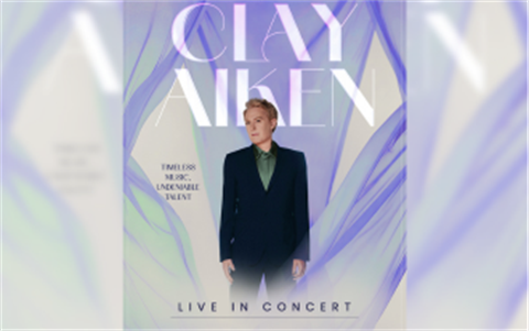 Clay Aiken stands in a dark navy suit against a soft lavender and blue background with flowing, translucent fabric. The concert poster features his name in large lettering and the tagline “Timeless Music, Undeniable Talent,” with “Live in Concert” at the bottom.
