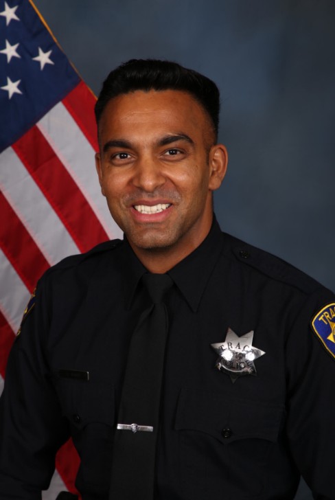 Tracy Police Officer Singh poses for an official department portrait in uniform with an American flag displayed in the background.
