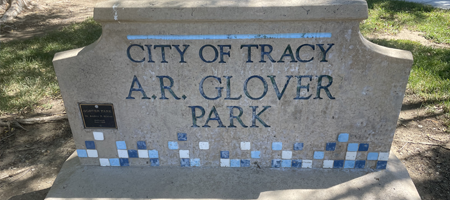 Stone sign reading ‘City of Tracy A.R. Glover Park’ with decorative blue and white tiles along the bottom.