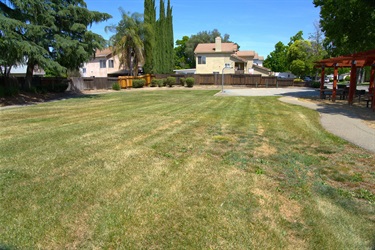 An open grassy lawn in a park, with houses and trees lining the background under a partly cloudy sky.