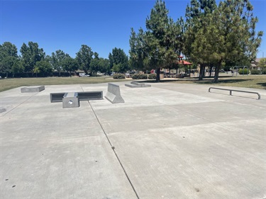Concrete skate park with ramps and ledges, surrounded by trees and a grassy area.