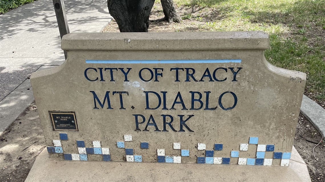 Stone entrance sign reading 'City of Tracy, Mt. Diablo Park' with a blue tile mosaic border and a small plaque, with greenery in the background.