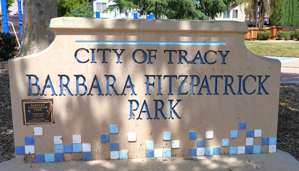 A stone monument sign with a decorative blue tile mosaic border reading 'City of Tracy, Barbara Fitzpatrick Park.'