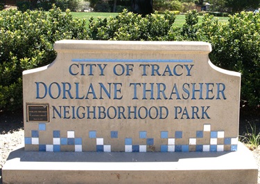 A stone monument sign with a decorative blue tile mosaic border reading 'City of Tracy, Dorlane Thrasher Neighborhood Park,' with a small plaque on the left side.
